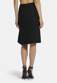 Zwarte kokerrok met verticale streepjes, kniehoogte, met een rits aan de achterkant. Draag met zwarte pumps met bandjes.