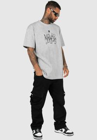 Grå bomuld t-shirt med sort grafisk design, parret med løstsiddende sorte cargo-bukser med flere lommer og sort-hvide sneakers.