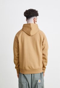 Brown hooded sweatshirt with a textured finish, featuring a relaxed fit and ribbed cuffs. Visible seams and a kangaroo pocket design.