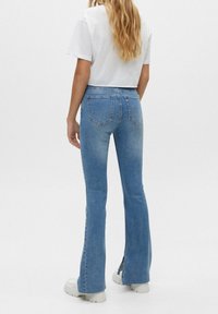 Blue high-waisted flared jeans with slight distressing, featuring classic pockets and a clean hem. Paired with a simple white cropped shirt.