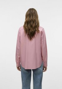 Camisa de manga larga rosa claro con puños de botón, corte relajado y dobladillo ligeramente curvado, combinada con pantalones vaqueros de pierna ancha azul claro.