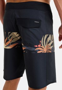 Bañador negro con un estampado tropical en naranja, beige y verde oscuro. Rayas texturizadas en la tela principal y un bolsillo en la parte trasera.