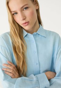 Light blue button-up shirt made of soft fabric, featuring a collar and long sleeves, with a smooth texture and matching buttons.