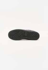 Svart sneakersåle med en teksturert gummi yttersåle, med bølgemønstre og spor for grep. Flate og avrundede kanter.