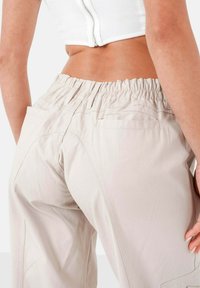 Lichtbeige broek met een elastische tailleband, voorzien van zijzakken en subtiele stikseldetails. Soepele textuur en een comfortabele pasvorm.
