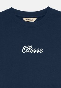 T-paita, jossa on lyhyet hihat, tummansininen ja valmistettu puuvillasta. Etupuolella kauluksen lähellä on valkoinen, kursivoitu "Ellesse"-logo.