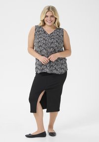 Blouse sans manches noir et blanc avec des rayures verticales, associée à une jupe noire au genou avec une fente sur le côté, portée avec des ballerines noires.