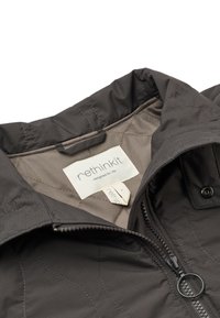 Gros plan sur le col d’une veste noire avec une fermeture éclair et une étiquette blanche visible indiquant "rethink kit designed for life."