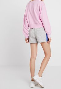 Rosa kortärmad sweatshirt med långa ärmar, kombinerad med grå texturerade shorts. Vita sportskor fulländar outfiten.