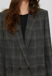 Blazer à carreaux gris avec un design croisé, des revers à pointe et deux poches avant. Tissu texturé avec des accents marron clair.