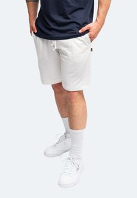 Pantaloni corti bianchi realizzati in tessuto morbido, con vita regolabile tramite cordino. Abbinati a sneakers bianche e calze bianche alte fino al ginocchio.