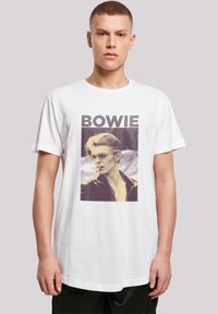 White cotton t-shirt featuring a graphic print of a person in sunglasses and a black jacket, with "BOWIE" text above in bold letters.