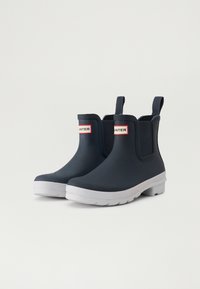 Botas de agua de náutico con suelas blancas, paneles laterales elásticos y una etiqueta de logo en rojo y blanco en la parte delantera. Textura suave, punta redondeada.