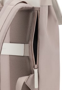 Zaino in tessuto texturizzato rosa chiaro con interno scuro, dotato di tasca con zip e dettagli in pelle bianca per resistenza e stile.
