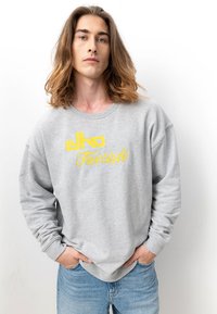 Grauer Sweatshirt mit gelbem "elko Freestyle"-Schriftzug, Rundhals, langen Ärmeln und lockerer Passform, kombiniert mit blauen Jeans.