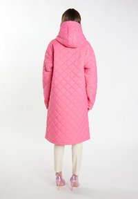 Cappotto lungo imbottito rosa con cappuccio, caratterizzato da un motivo a diamante. Il cappotto è abbinato a pantaloni color crema e tacchi alti rosa lucidi.