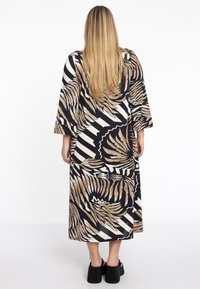 Maxikleid mit auffälligem schwarz-beige-blumigen Muster und Streifen, langen Ärmeln und lockerer Passform. Kombiniert mit klobigen Plateauschuhen.