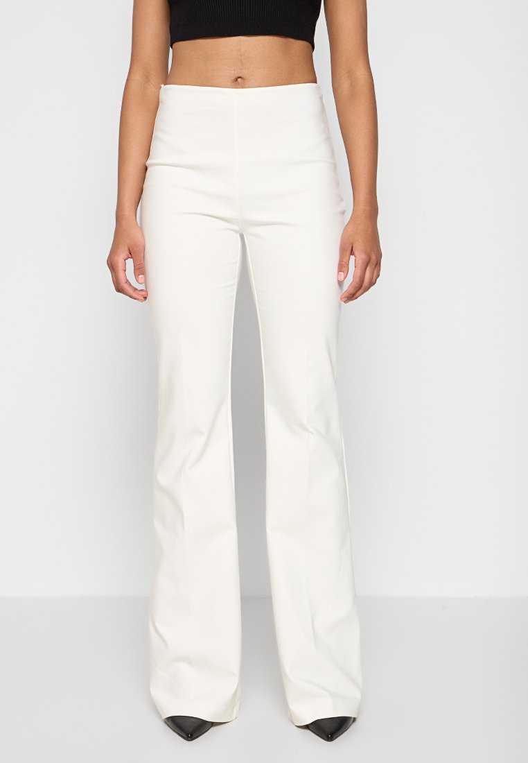 Weiße Schlaghosen mit glatter Textur; hoch tailliertes Design; kombiniert mit schwarzen spitzen High Heels; minimalistischer Stil.