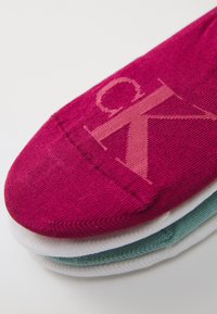 Meias de tornozelo multicoloridas com uma cor rosa dominante, apresentando um logótipo rosa claro. O design inclui uma textura suave e detalhes de costura subtis.