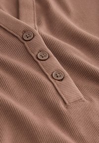 Tessuto a coste marrone con tre bottoni rotondi di un marrone scuro lungo una placca. Texture morbida con un sottile motivo a strisce verticali.