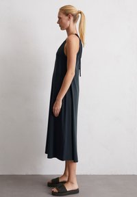 Schwarzes ärmelloses Kleid mit entspannter Passform, das hinten einen Bindeband hat und einen knielangen Saum aufweist, kombiniert mit dunkel gewebten Rutschsandalen.