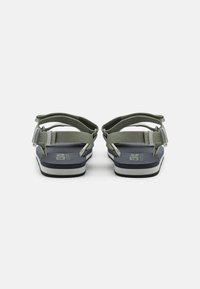 Green adjustable sandals with a textured strap design, thick navy sole, and white accent band. Durable materials for outdoor use.