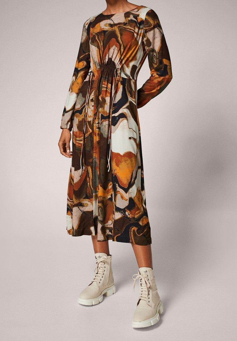Femme portant une robe midi à manches longues avec un motif abstrait multicolore et des bottines beige à lacets.