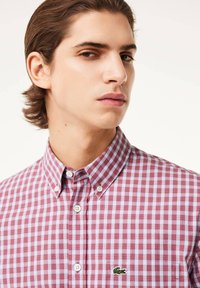 Camisa de cuadros roja y azul de gingham con cuello clásico, cierre de botones y logo de cocodrilo bordado en el bolsillo izquierdo del pecho.