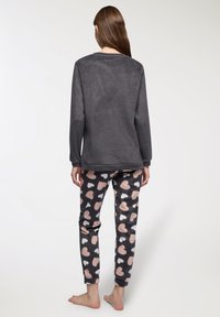 Felpa grigia a maniche lunghe con scollatura rotonda abbinata a pantaloni neri con un motivo a cuori rosa e bianco. A piedi nudi, vista da dietro.