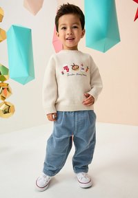 Pull en tricot crème avec broderies festives et pantalon en velours côtelé bleu clair, doté d'une coupe décontractée et de poignets en maille. Des baskets blanches viennent compléter la tenue.