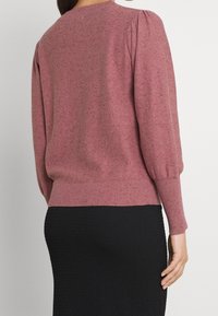 Rosa strukturierter Pullover mit gepufften Ärmeln und einem gerippten Saum. Verfügt über eine lockere Passform und ein dezentes Sprenkelmuster. Schwarzer Rock sichtbar.