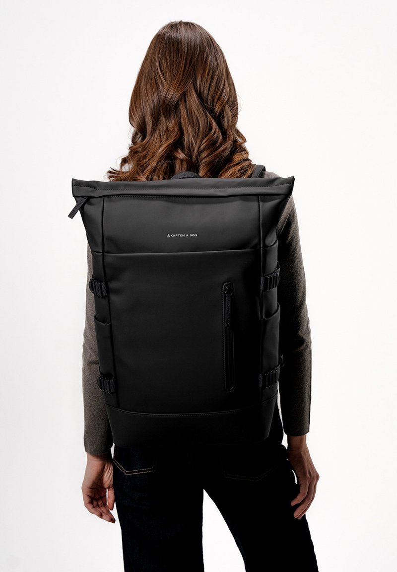 Zaino roll-top nero realizzato in tessuto resistente, dotato di spallacci regolabili, tasca frontale con zip, dettaglio del logo e un design strutturato e minimalista.