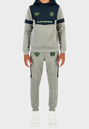 Grijs sporttrainingspak met zwarte accenten, bestaande uit een hoodie en taps toelopende broek. Opvallende details zijn groene logo's en patronen.