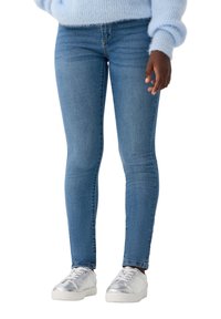 Chude niebieskie dżinsy o gładkiej fakturze i subtelnych przetarciach, zestawione ze srebrnymi trampkami. Prosty krój z standardowymi detalami szycia.