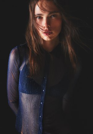 Transparante marineblauwe blouse met verticale strepen. Heeft een kraag en een knoopsluiting aan de voorkant, die de lichte stof en een subtiele glans benadrukken.
