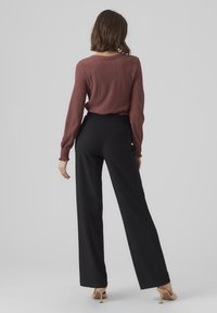 Top rustico a maniche lunghe e textura con polsini elasticizzati, abbinato a pantaloni neri a vita alta e gamba dritta, insieme a tacchi color beige.