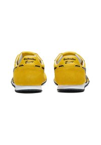 Žluté semišové sportovní boty s černými detaily, s nízkým profilem, zaoblenou patou a logem na patní části.