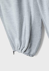 Hellgraue Jogginghose mit elastischem Bündchen und schwarzem verstellbarem Kordelzug vor weißem Hintergrund.