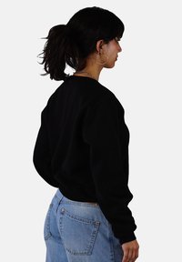 Black sweatshirt with a crew neck, relaxed fit, and ribbed cuffs, paired with light blue jeans featuring back pockets and copper rivets.