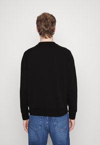 Felpa nera con collo rotondo, polsini a costine e vita aderente, abbinata a jeans azzurri chiari, vista da dietro.