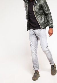 Grøn puffjakke med en shiny finish, sort crew neck skjorte, lysegrå jeans og olivengrønne sneakers. Casual outfit med en afslappet pasform.