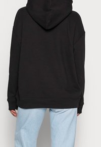 Sudadera negra de gran tamaño con una amplia capucha, corte holgado, puños y dobladillo acanalados. Combinada con unos vaqueros de corte relajado en azul claro.