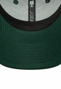 Dunkelgrüner Baseballcap mit schwarzem Rand und genähten, runden Belüftungslöchern auf dem inneren hellgrauen Stoff.