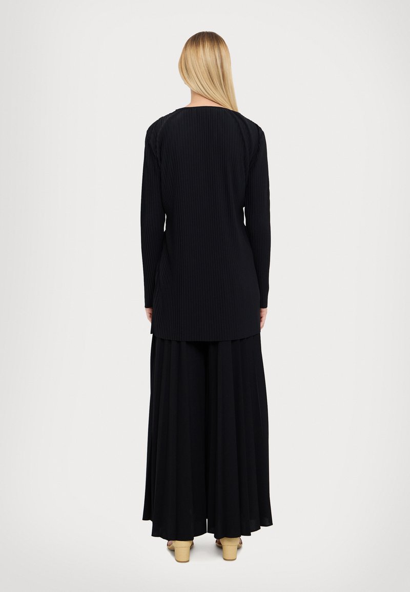 Langes schwarzes Rippenshirt mit einem runden Ausschnitt, kombiniert mit einem fließenden schwarzen Rock. Das Material scheint weich mit einer strukturierten Oberfläche zu sein.