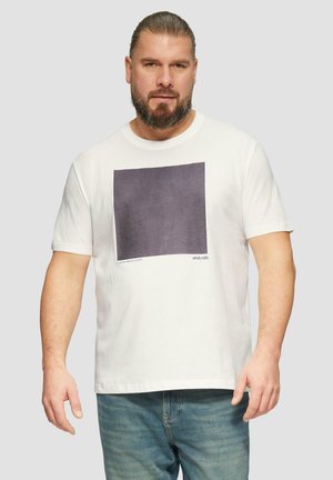 Witte katoenen t-shirt met een donkere vierkante grafische print op de voorkant, ronde halslijn en korte mouwen. In combinatie met lichtblauwe jeans.