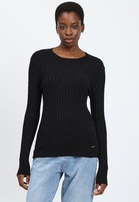 Maglione a costine nero con maniche lunghe, scollatura rotonda e sottile accento del marchio sull'orlo. Texture liscia, silhouette aderente.