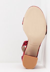 Sandale à talon haut à imprimé léopard rouge avec un dessus texturé et une semelle nude lisse. Présente une large sangle sur le pied et un talon arrière.