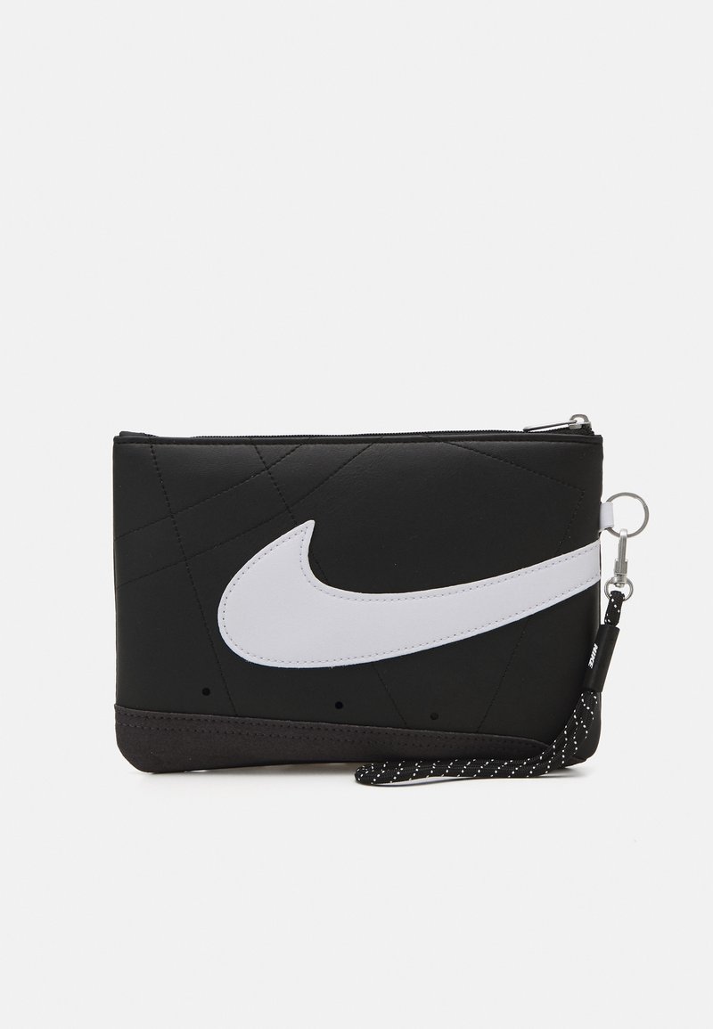 Pochette noire zippée avec grand logo swoosh blanc et sangle noire à pois blancs attachée à un porte-clés en métal.