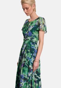 Sukienka w kwiatowy wzór w odcieniach zieleni, niebieskiego i fioletu; krótkie, falbaniaste rękawy; dopasowana góra; zwiewna spódnica z zakładkami.