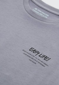 Graues, oversized T-Shirt mit Rundhalsausschnitt. Mit schwarzem Text "EASY LIFE!" und zusätzlichen Phrasen darunter in einer lässigen Schriftart.